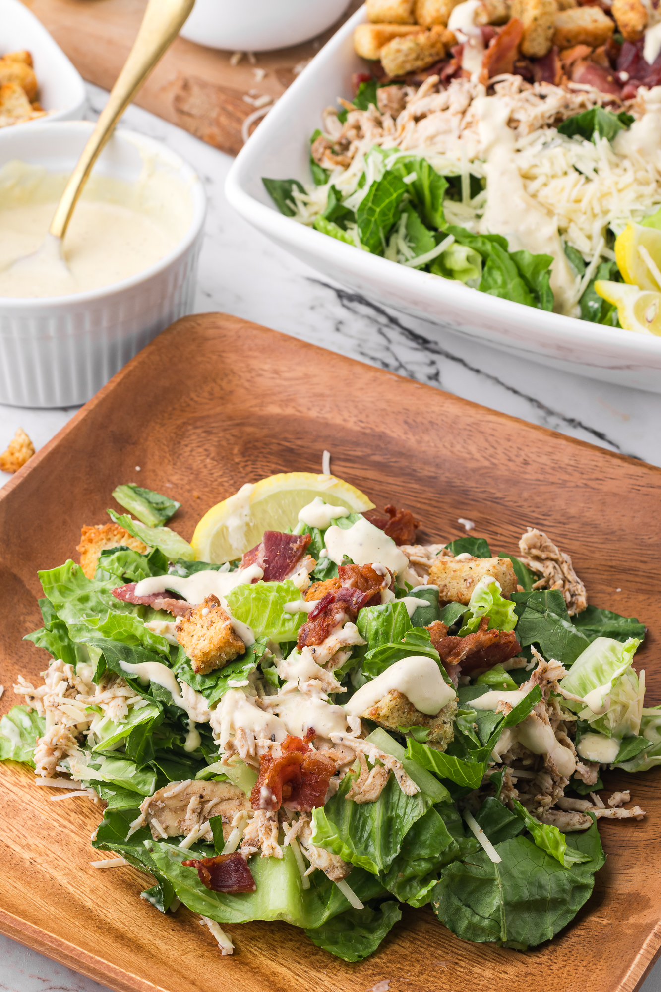 A wooden plate of Chicken Bacon Caesar Salad.