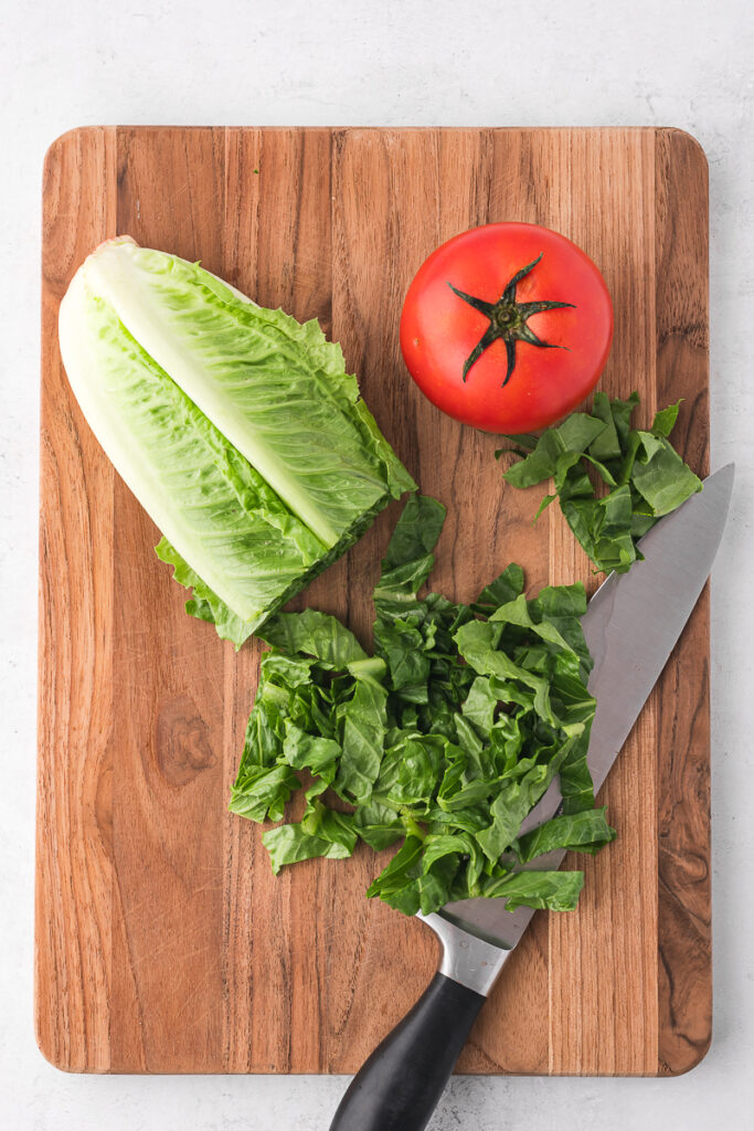 Romaine and a tomato on a wooden cutting board.