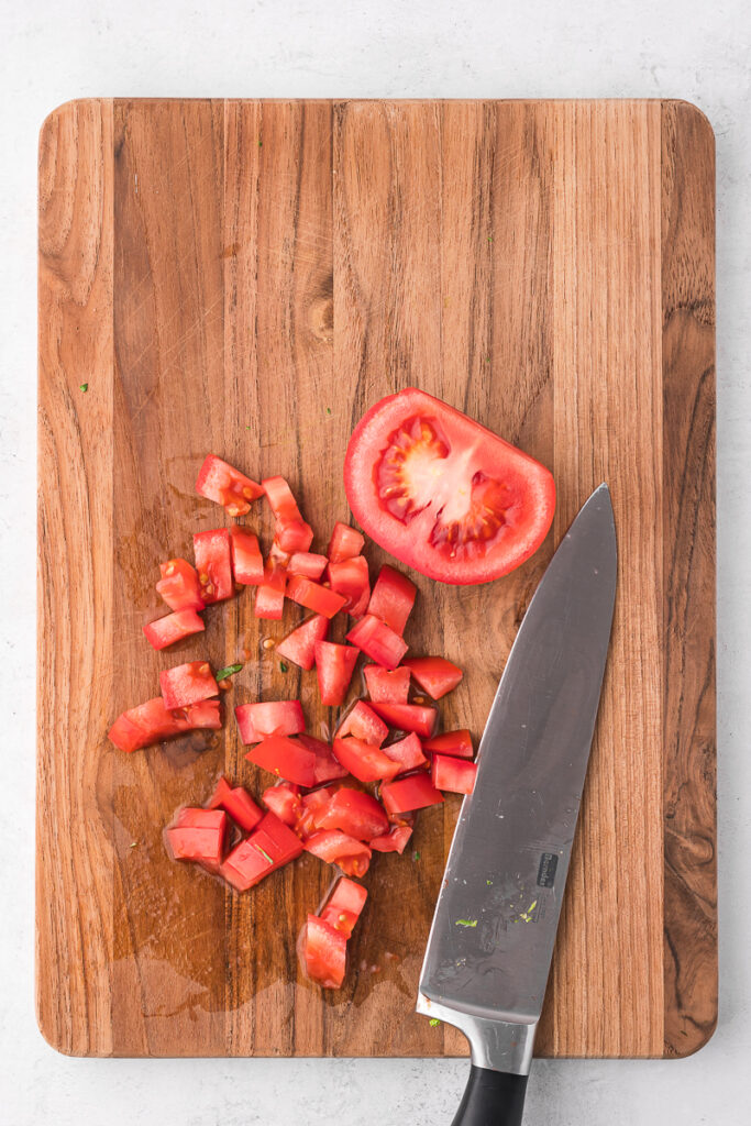 A half chopped tomato on a wooden cutting board.