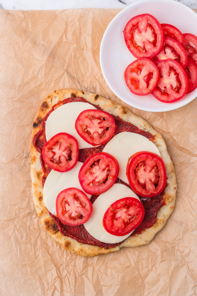 A flatbread covered with tomato sauce, mozzarella cheese, and tomatoes.