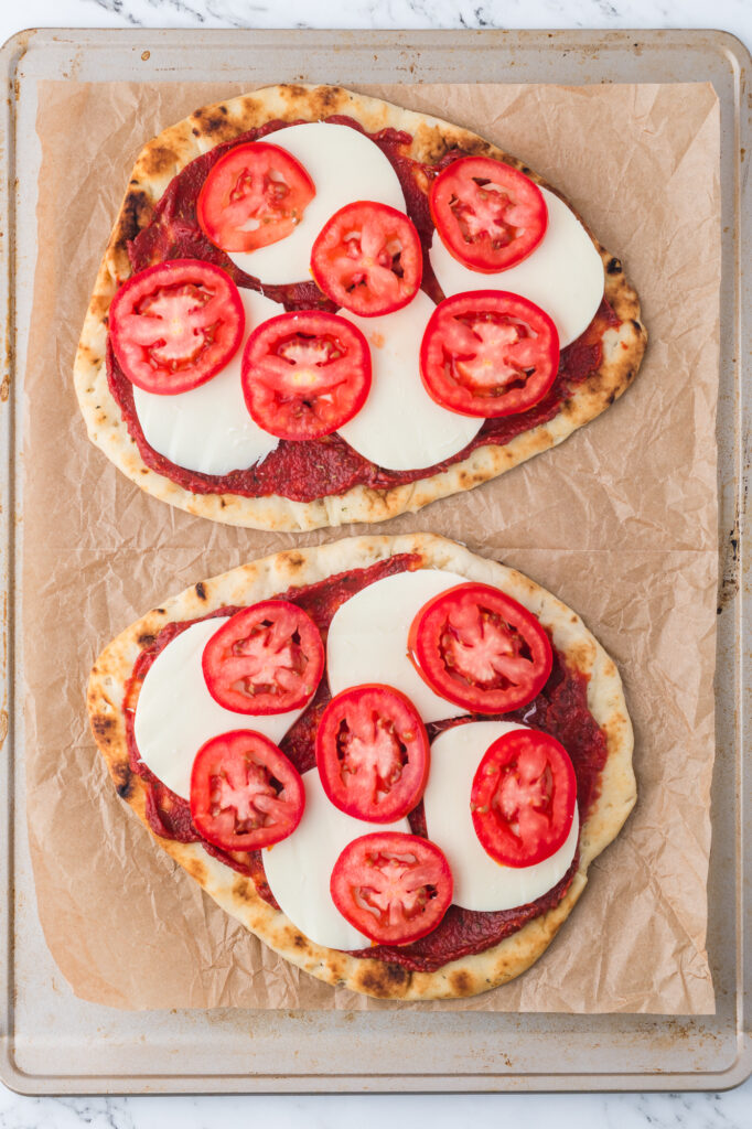 Two flatbreads covered with tomato sauce, mozzarella cheese, and tomatoes.