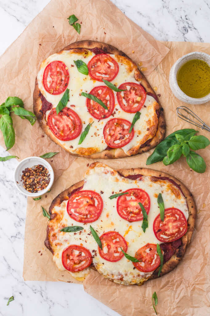 Two baked flatbreads covered with tomato sauce, mozzarella cheese, tomatoes, and topped with basil.