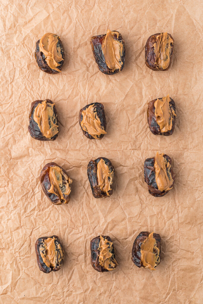 A piece of parchment paper holding 12 pitted dried dates stuffed with peanut butter.