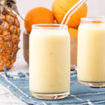 A clear glass of Pineapple Orange Smoothie with a glass straw in it.