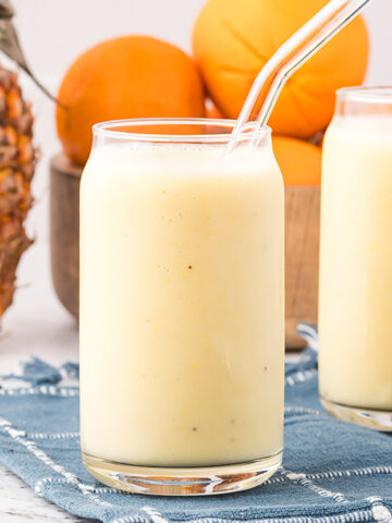 A clear glass of Pineapple Orange Smoothie with a glass straw in it.