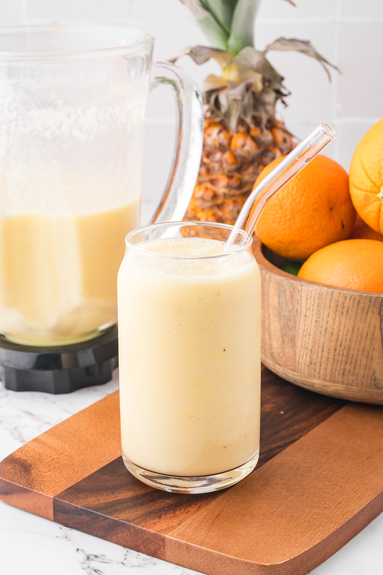 A Pineapple Orange Smoothie in a glass with a glass straw.