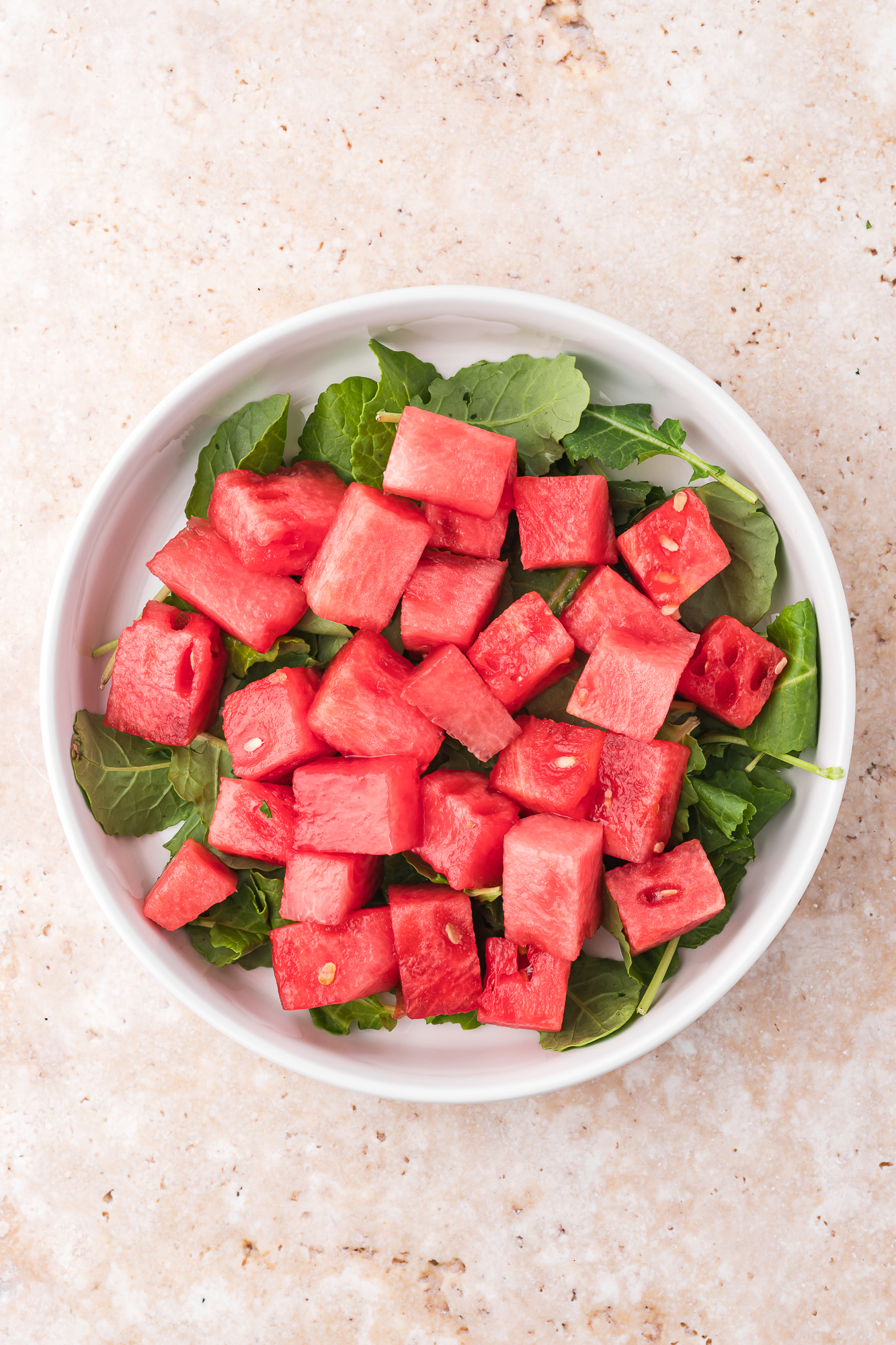 Cubed watermelon on a bed of baby kale in a white bowl.