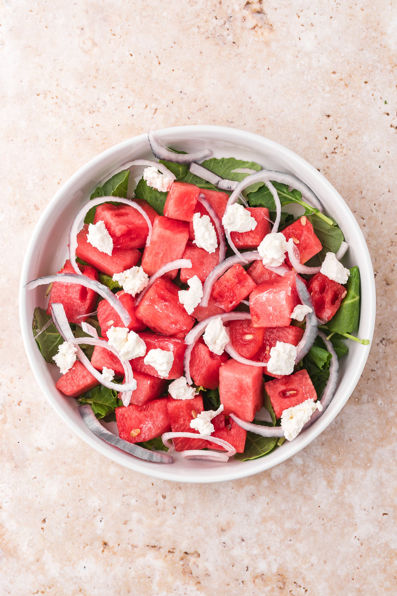 A white bowl containing undressed Watermelon Goat Cheese Salad.