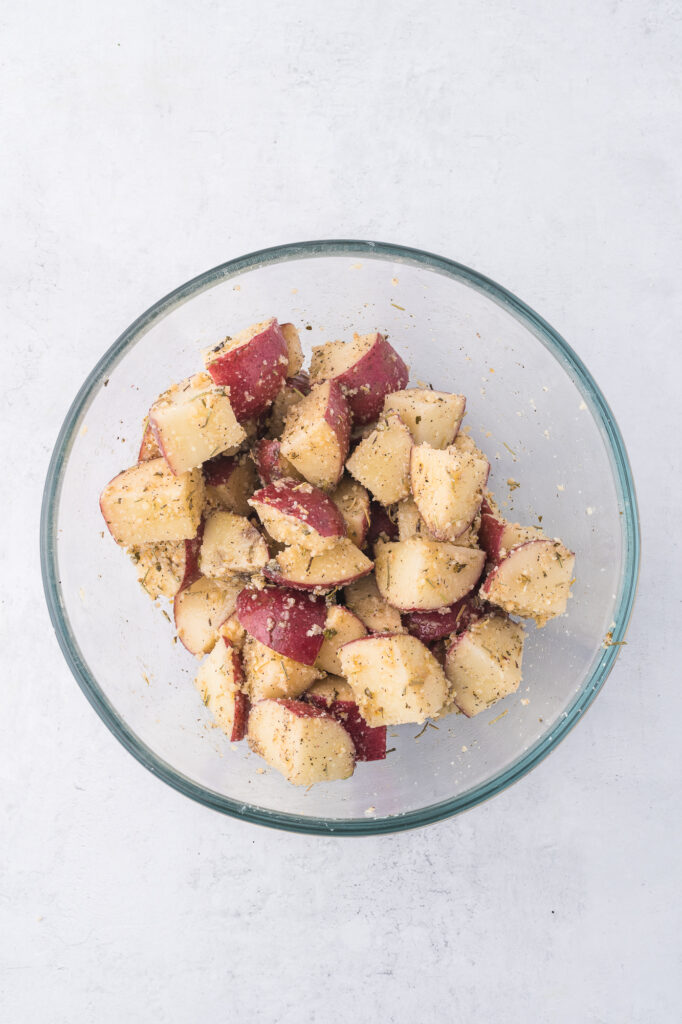 A bowl of cut up raw red potatoes mixed with all the seasonings.