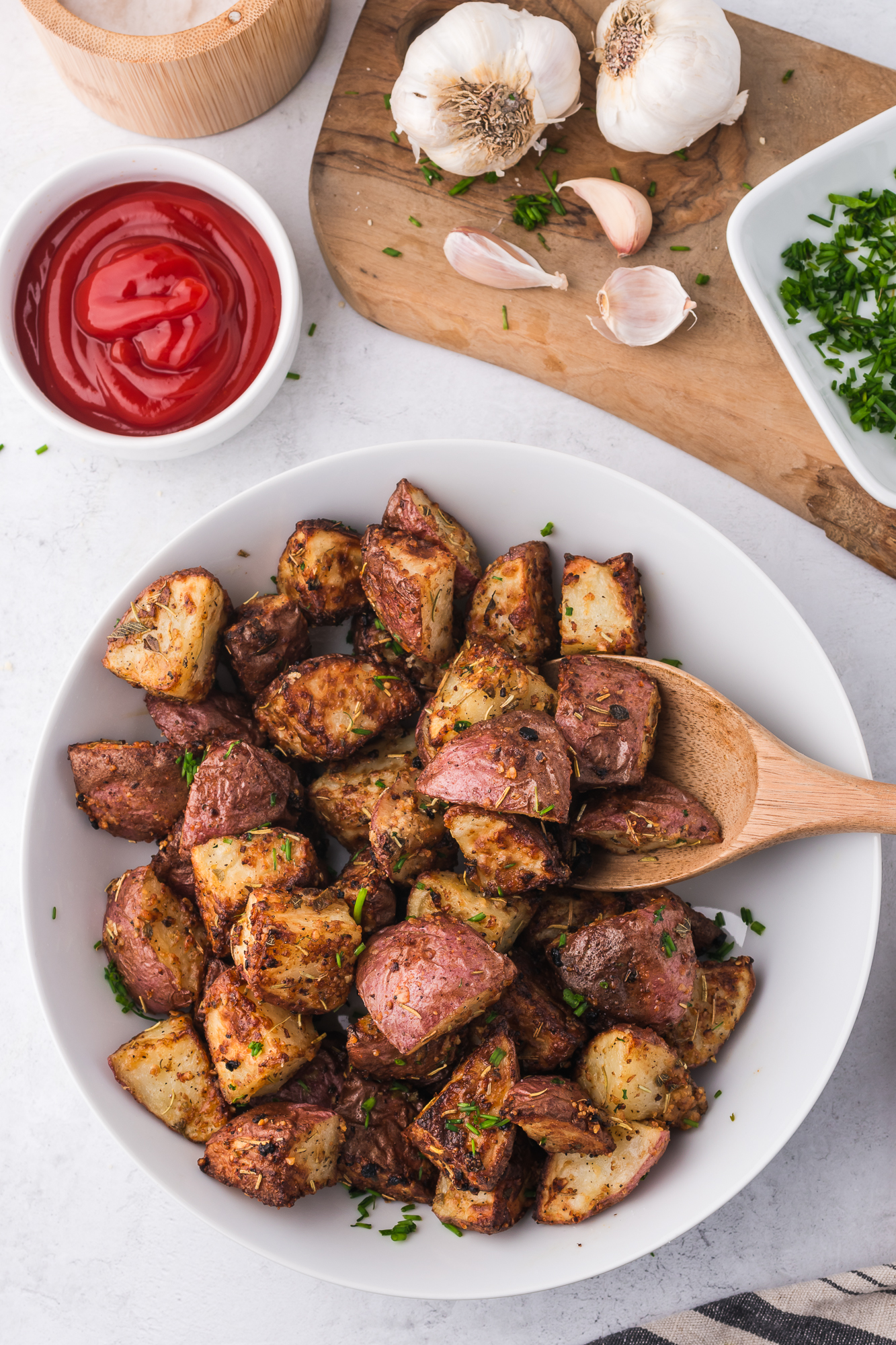 A white bowl with Air Fryer Red Potatoes and a wooden spoon.