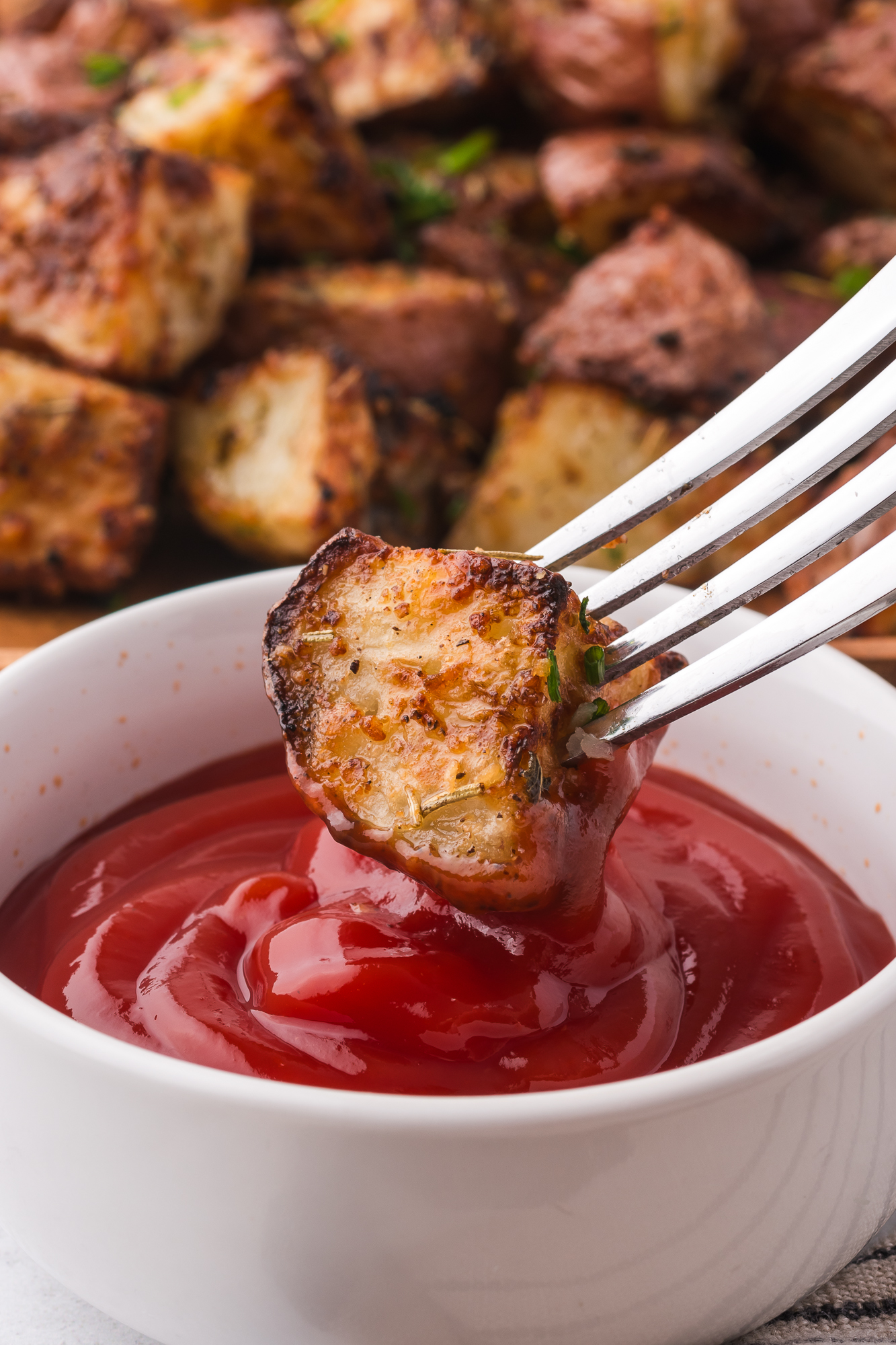 A close-up of one piece of Air Fryer Red Potatoes being dipped into ketchup with a fork.