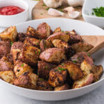 A white bowl of Air Fryer Red Potatoes with a wooden spoon in the bowl, too.