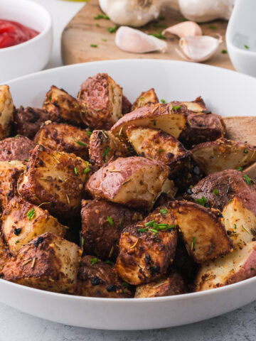 A white bowl of Air Fryer Red Potatoes with a wooden spoon in the bowl, too.