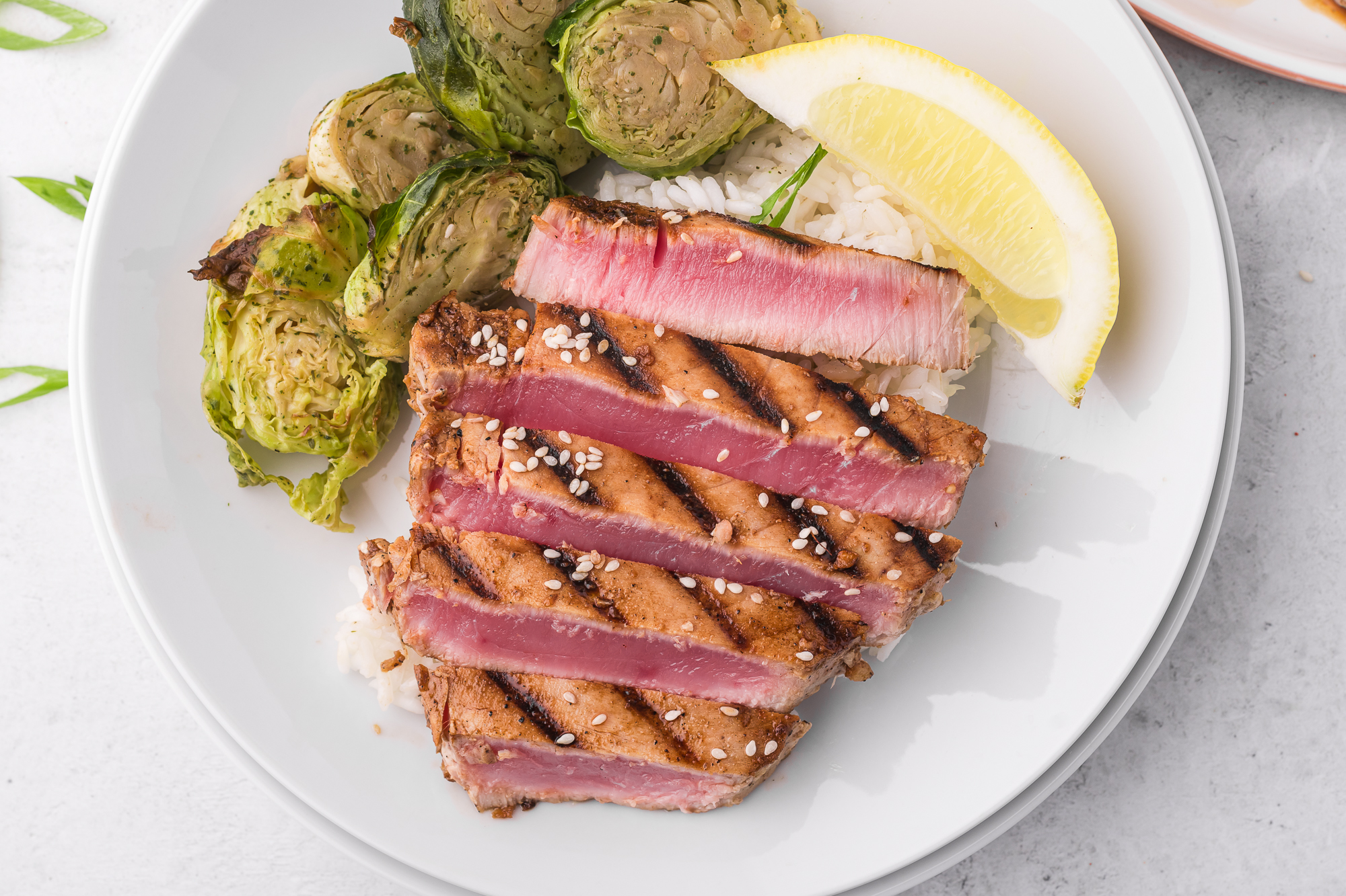 A plated sliced Grilled Tuna Steak with Brussels sprouts and a lemon wedge.