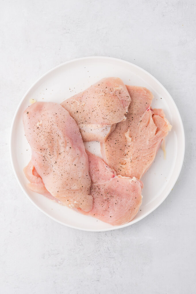 A plate of seasoned raw chicken breasts.