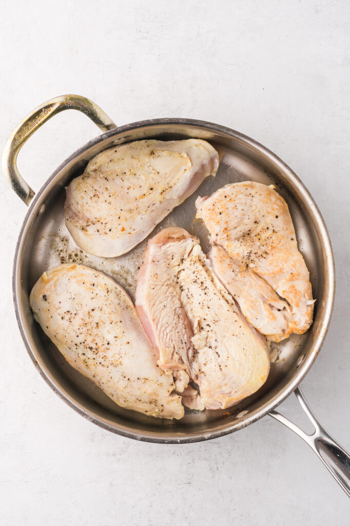 A pan of searing seasoned chicken breasts.