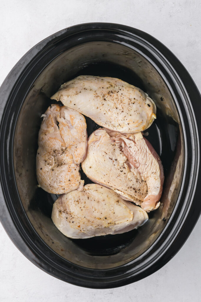 A slow cooker filled with seared chicken breast.