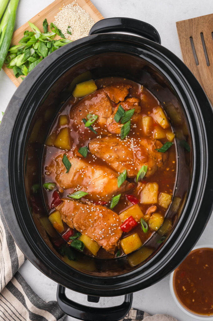 A slow cooker of cooked Slow Cooker Hawaiian Chicken with toppings.