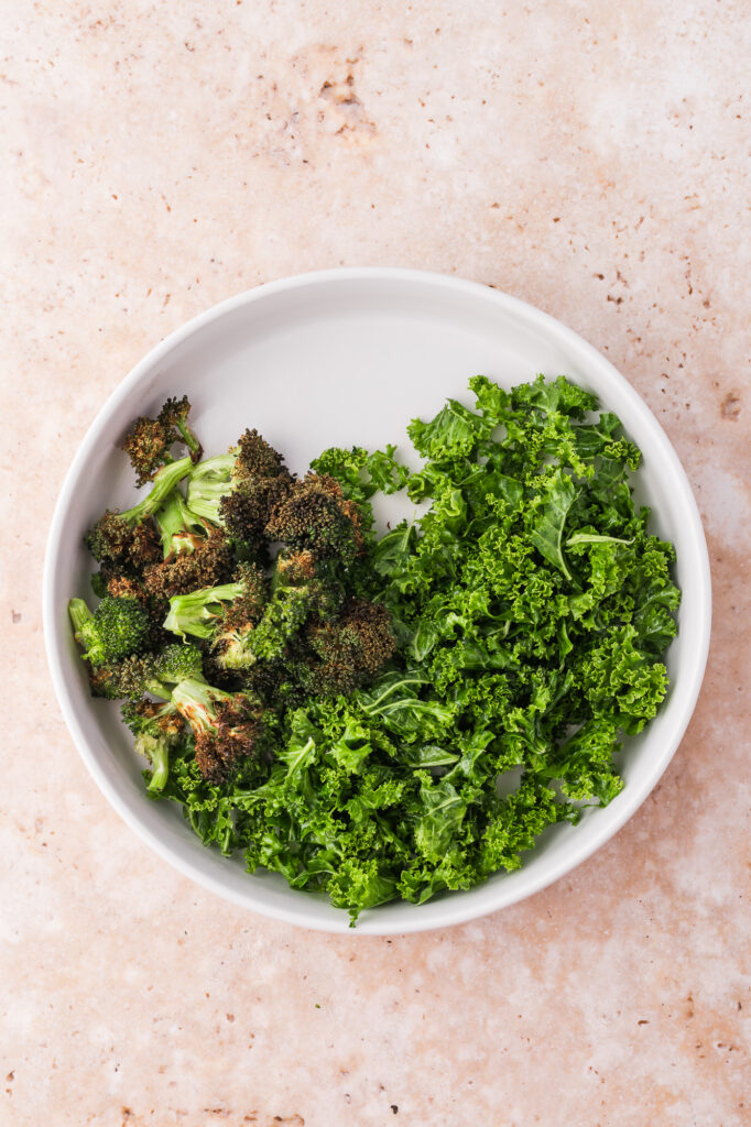 A white bowl with kale and roasted broccoli.