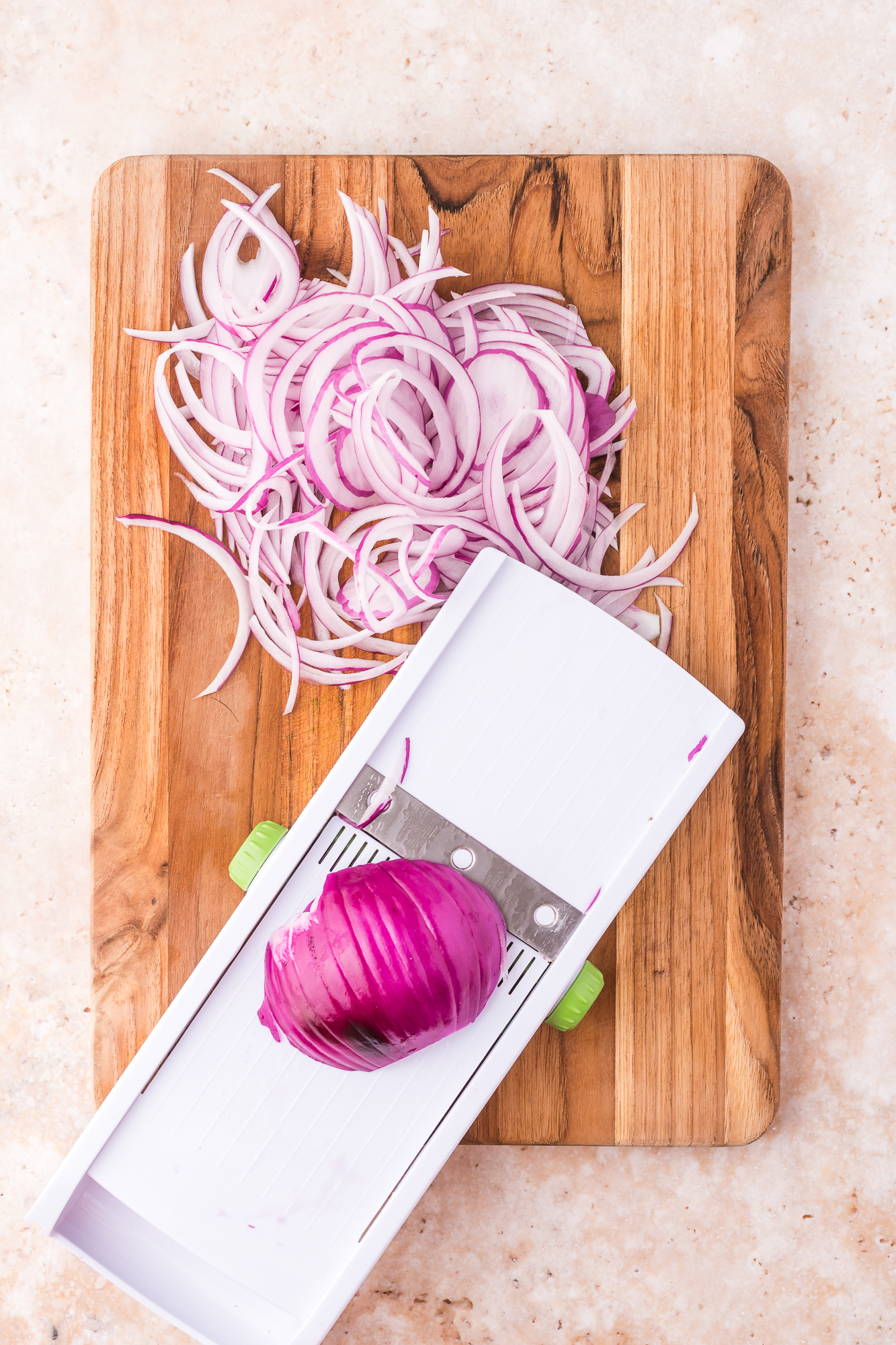 A mandolin slicer slicing raw red onions.