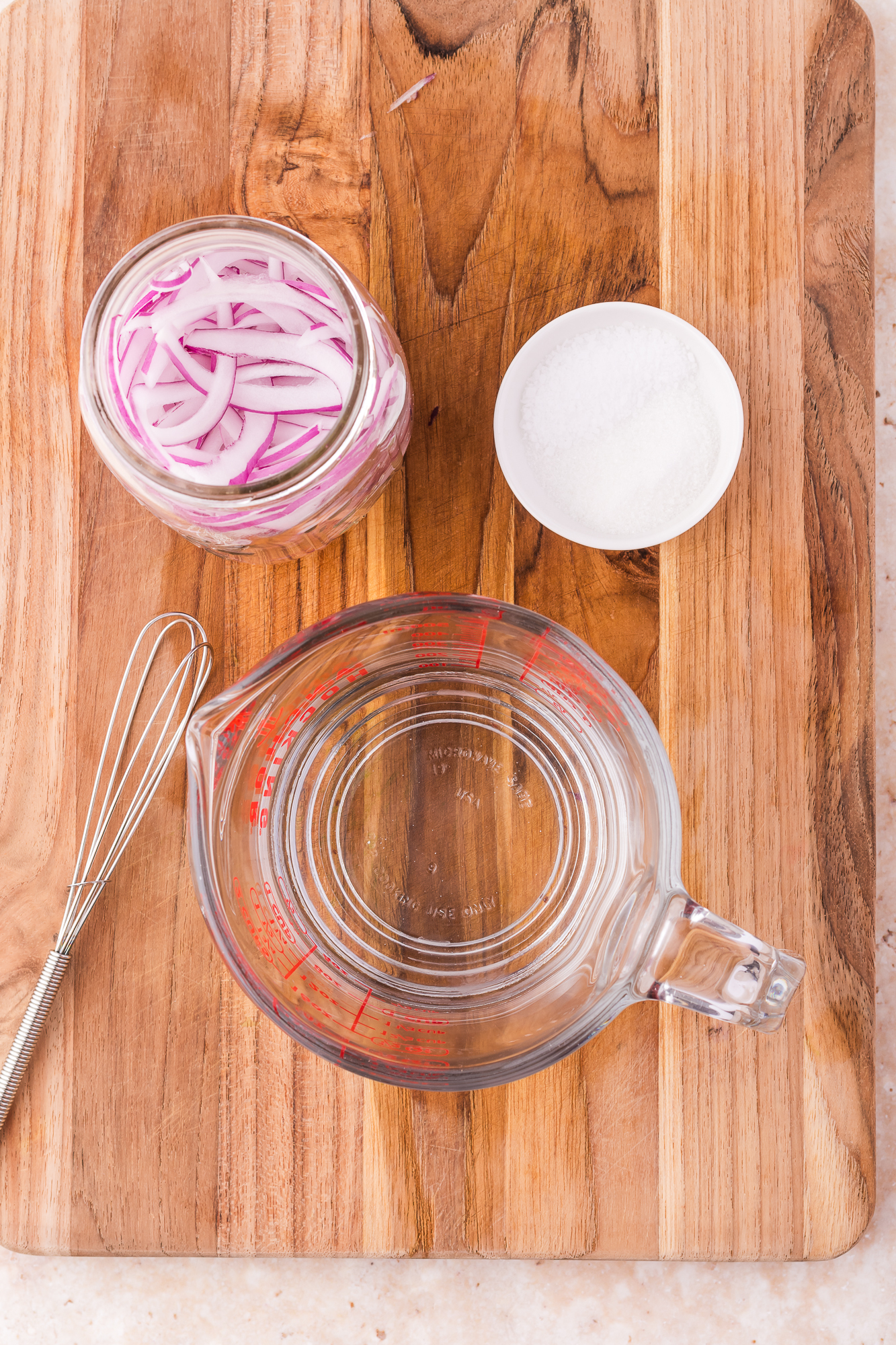 A jar of sliced onions next to measuring cup and a small whisk