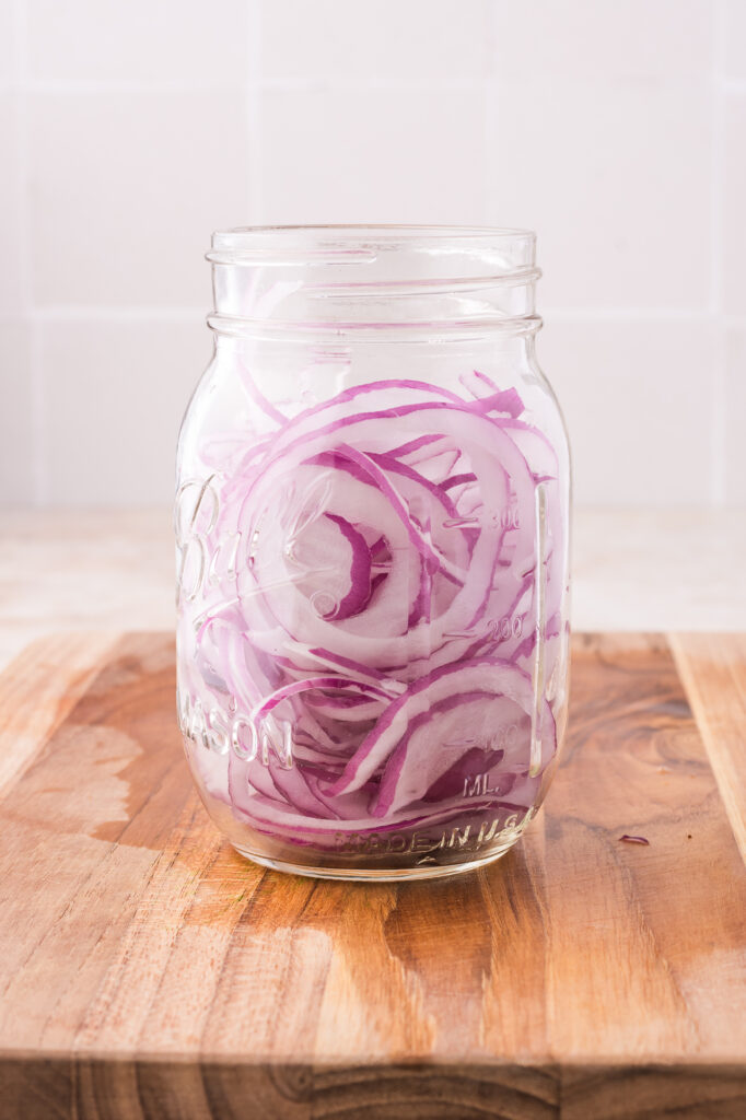 A mason jar of sliced raw red onions.