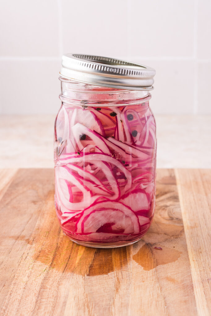 A mason jar of sliced raw red onions with covered in the brine.