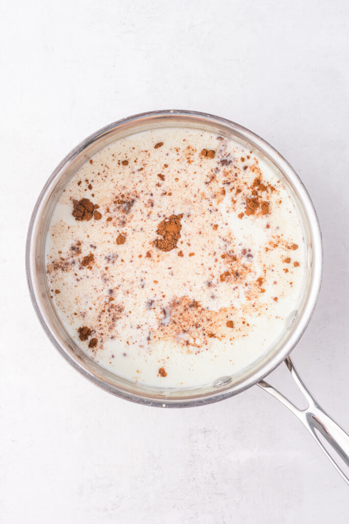 A saucepan of milk with cinnamon and other ingredients floating in it.