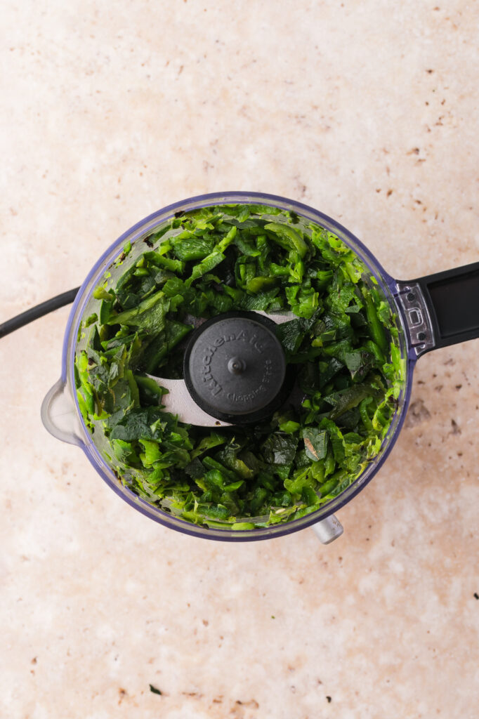 A food processor with processed charred poblano peppers for Smoky Poblano Ranch Dressing.