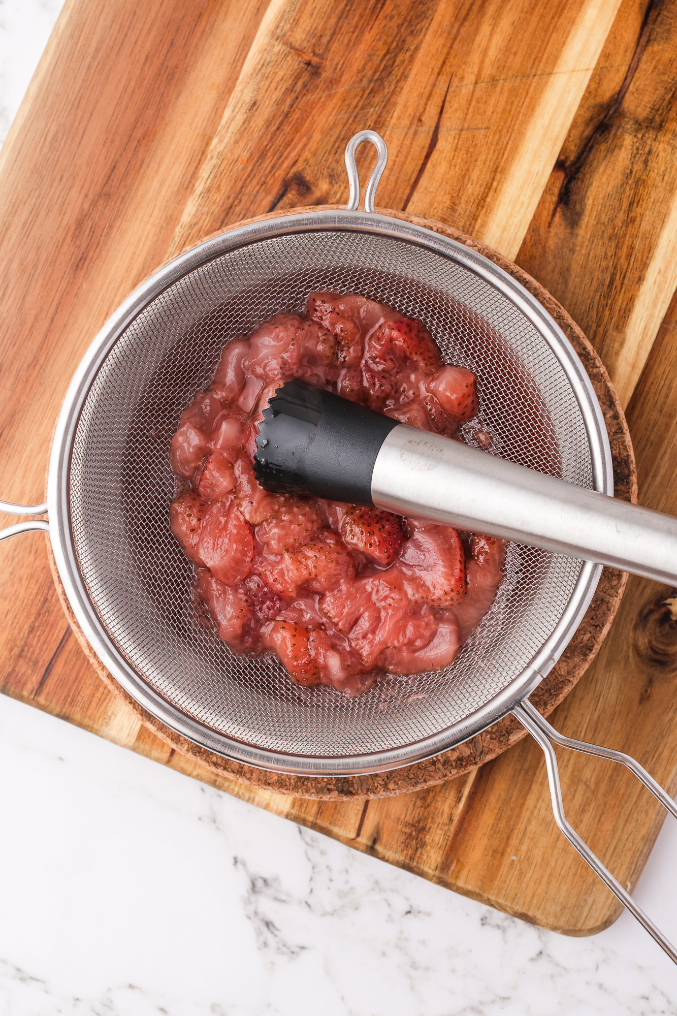 Cooked strawberries being put juiced through a sieve.