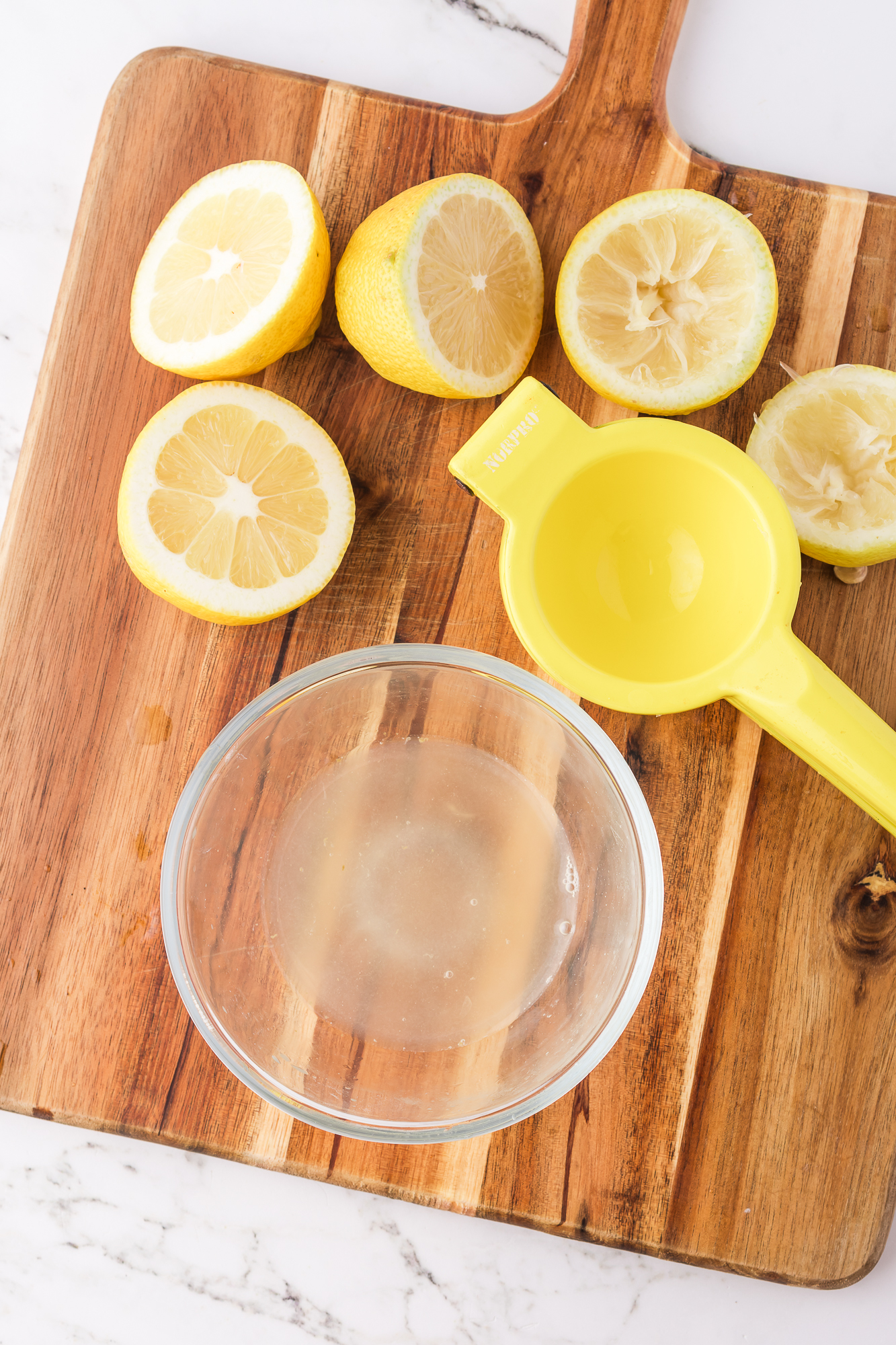 A citrus squeezer on a wooden cutting board next to some sliced lemons and a glass bowl of lemon juice.