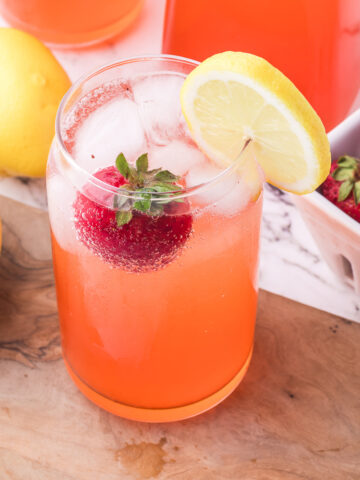 A glass of Sparkling Strawberry Lemonade with a whole strawberry and a slice of lemon on the rim.