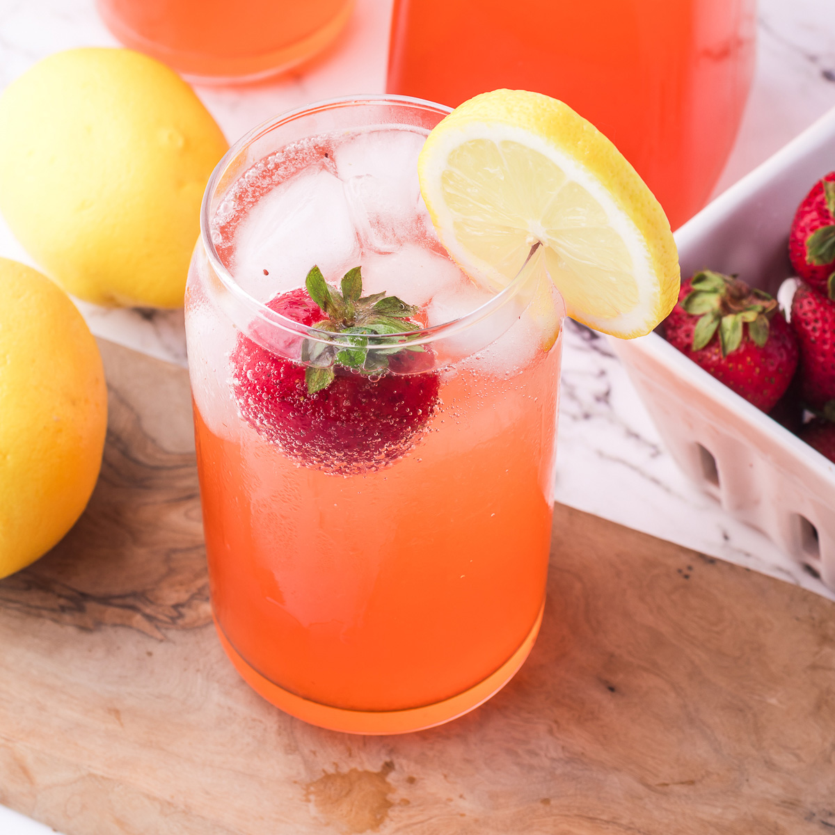 A glass of Sparkling Strawberry Lemonade with a whole strawberry and a slice of lemon on the rim.