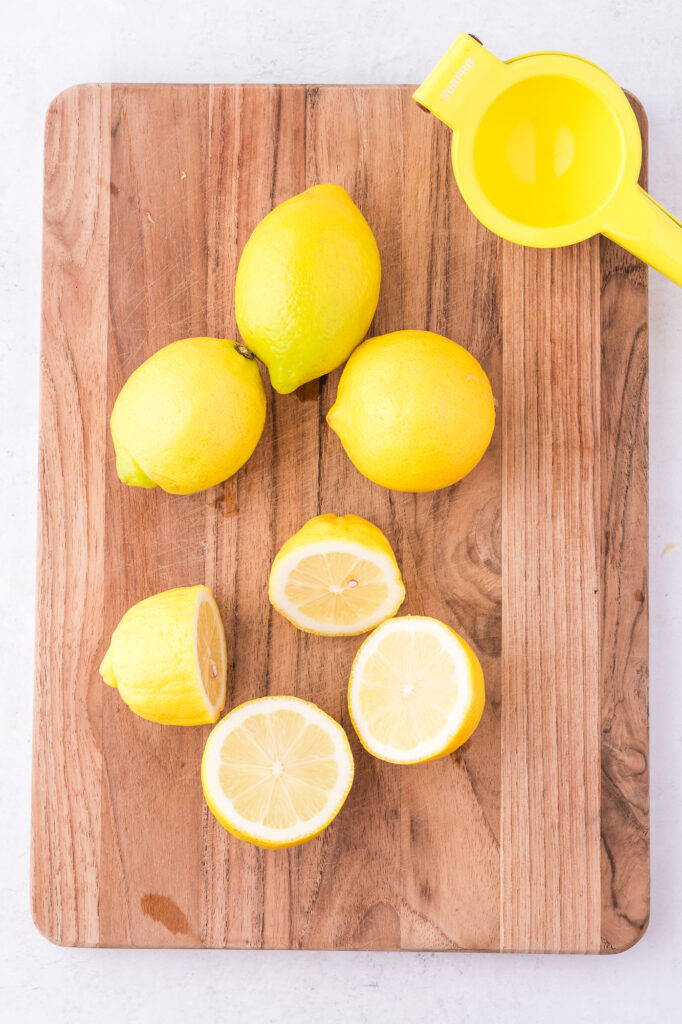 A wooden cutting board with 2 intact lemons and 2 that have been cut in have to make State Fair Lemonade.