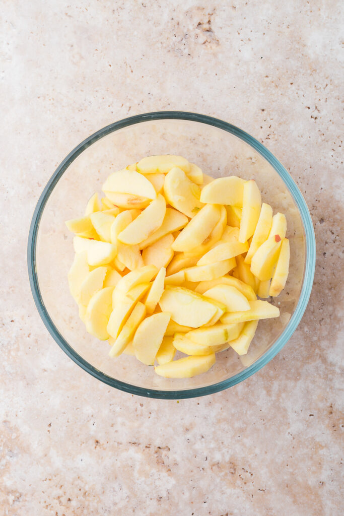 A glass bowl of peeled and sliced apples.