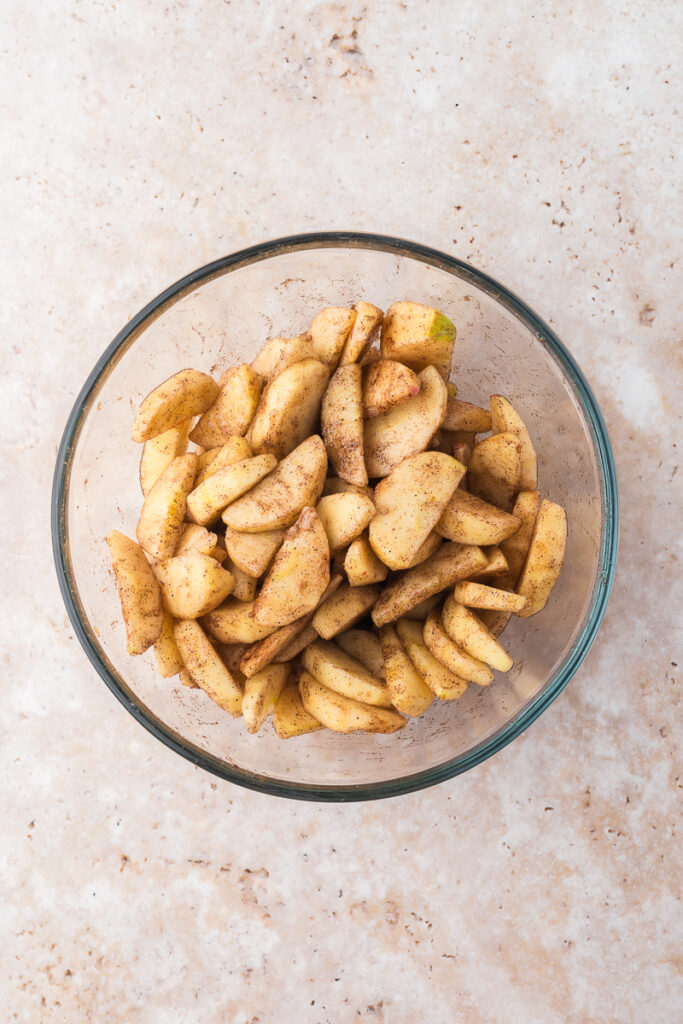 A glass bowl of peeled and sliced apples topped with the sauce.