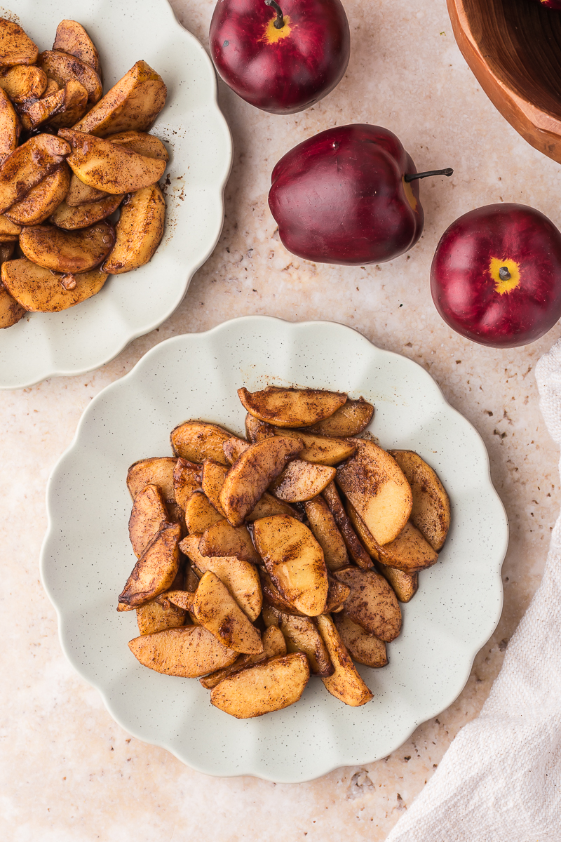 A plate of Air Fryer Apples with Bourbon surrounded by whole apples.