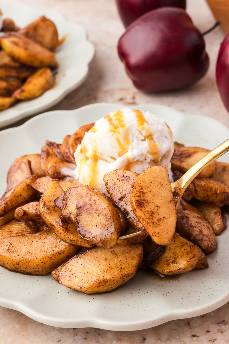 A close-up of a plate of Air Fryer Apples with Bourbon topped with vanilla ice cream, and a fork holding a few pieces.