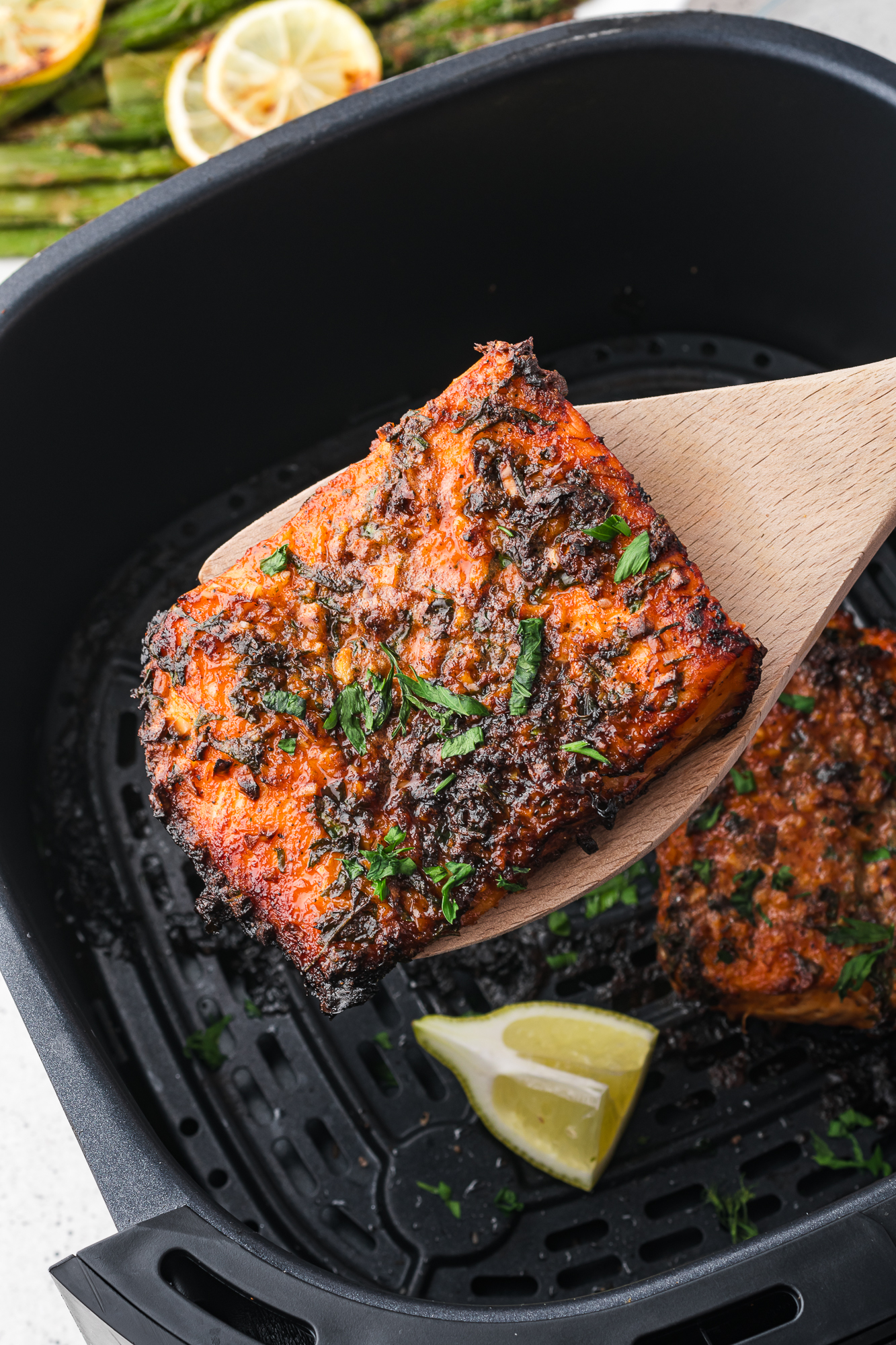 An Air Fryer Garlic Butter Salmon filet cooked in the air fryer behind held over the air fryer basket by a wooden sppon.