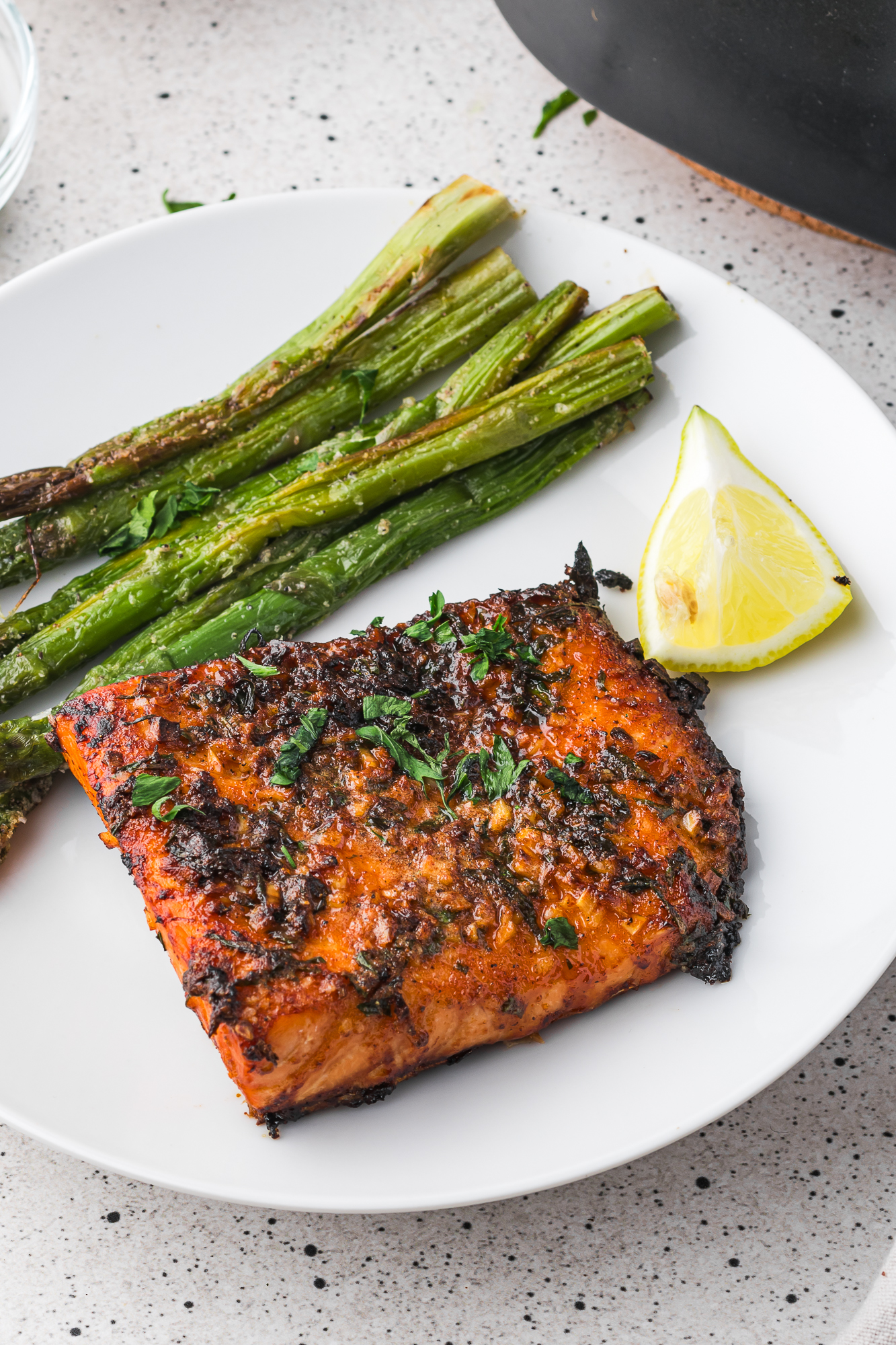 A plated Air Fryer Garlic Butter Salmon filet with a side of asparagus and a lemon wedge.