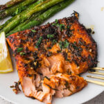 An Air Fryer Garlic Butter Salmon on a plate, slightly flaked off with a fork.