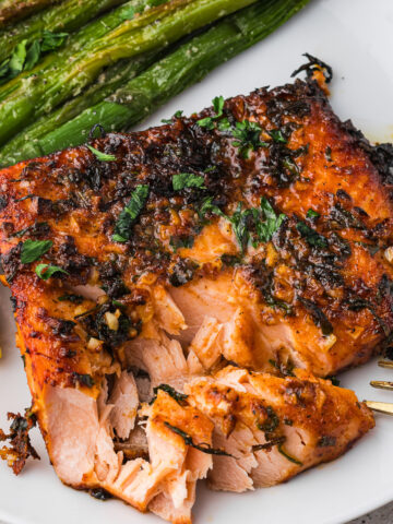 An Air Fryer Garlic Butter Salmon on a plate, slightly flaked off with a fork.