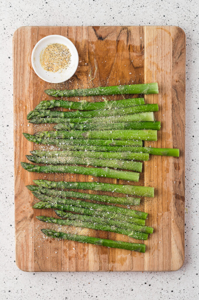 A cutting board with trimmed and coated asparagus on it.