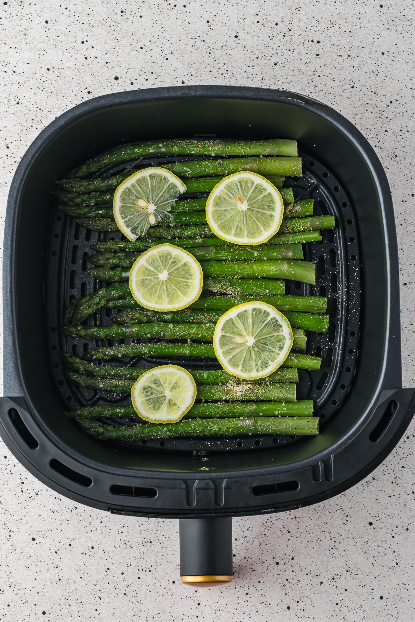 An air fryer basket with the pre-cooked Air Fryer Lemon Asparagus in it.