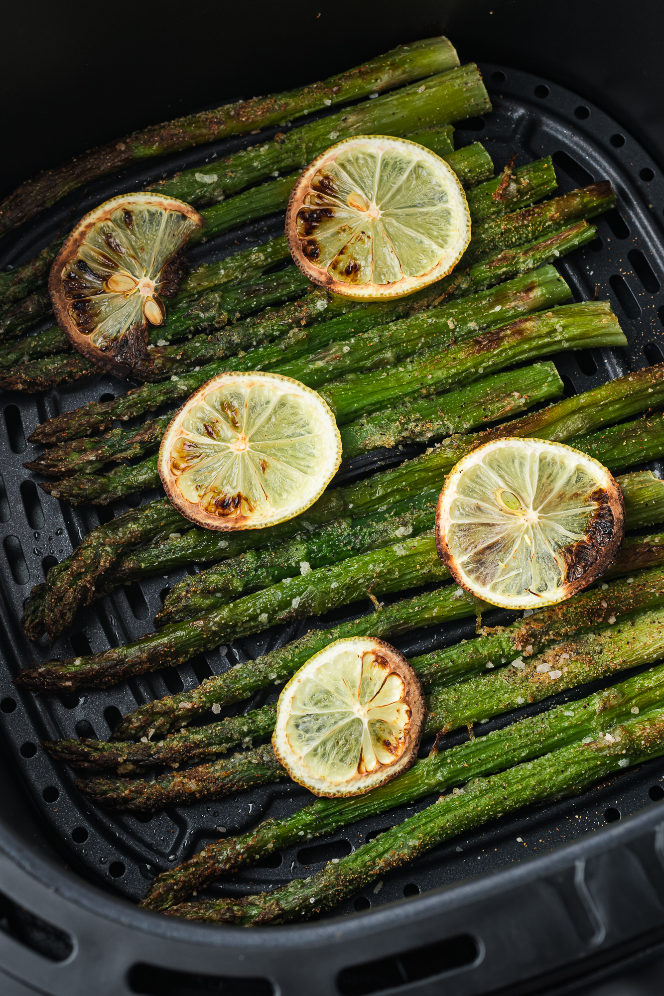 An air fryer basket with the cooked Air Fryer Lemon Asparagus in it.