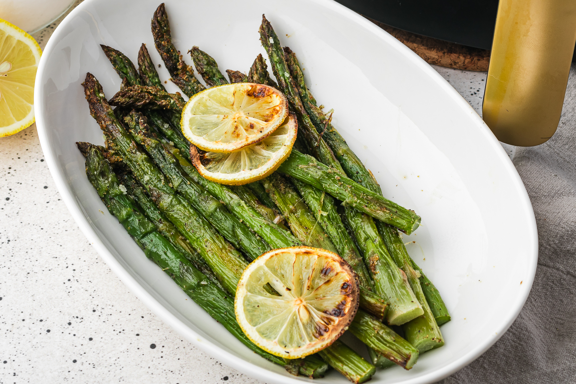 A white bowl of Air Fryer Lemon Asparagus with lemon slices as garnish.