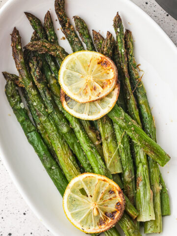 A plate of Air Fryer Lemon Asparagus with lemon slices on top as garnish.