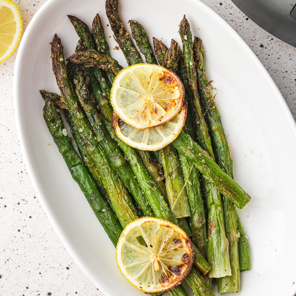 A plate of Air Fryer Lemon Asparagus with lemon slices on top as garnish.