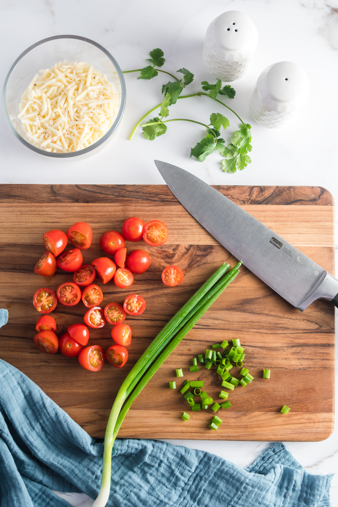 A cutting board with sliced scallions and cherry tomatoes sliced in half for Sweet Potato Breakfast Burritos.