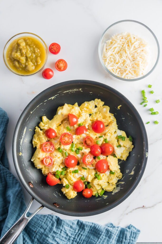 A pan of scrambled eggs with cherry tomatoes on top for Sweet Potato Breakfast Burritos,